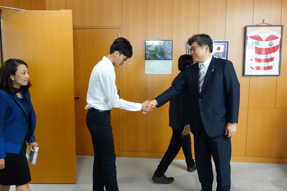 大臣室に入る学生に握手する萩生田大臣